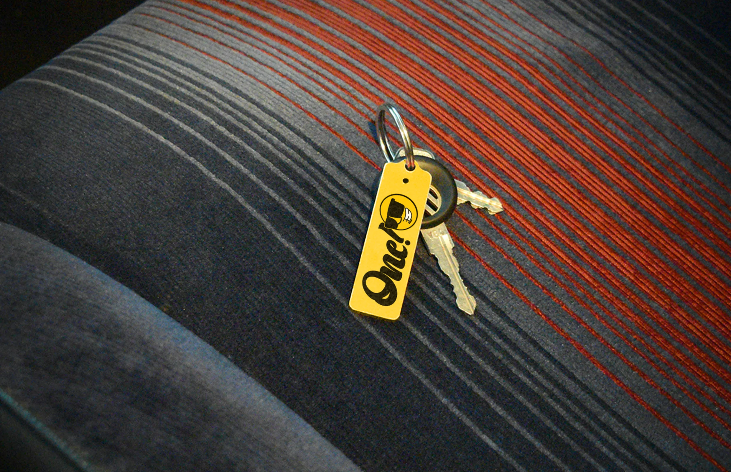 Llaves de auto con la etiqueta de One Car Rental sobre el asiento de un vehículo. Este diseño refuerza la identidad visual vibrante y memorable de la marca en el mercado de renta de autos turísticos. La combinación de colores llamativos y el logotipo único garantizan una presencia distintiva en el sector de transporte y turismo.