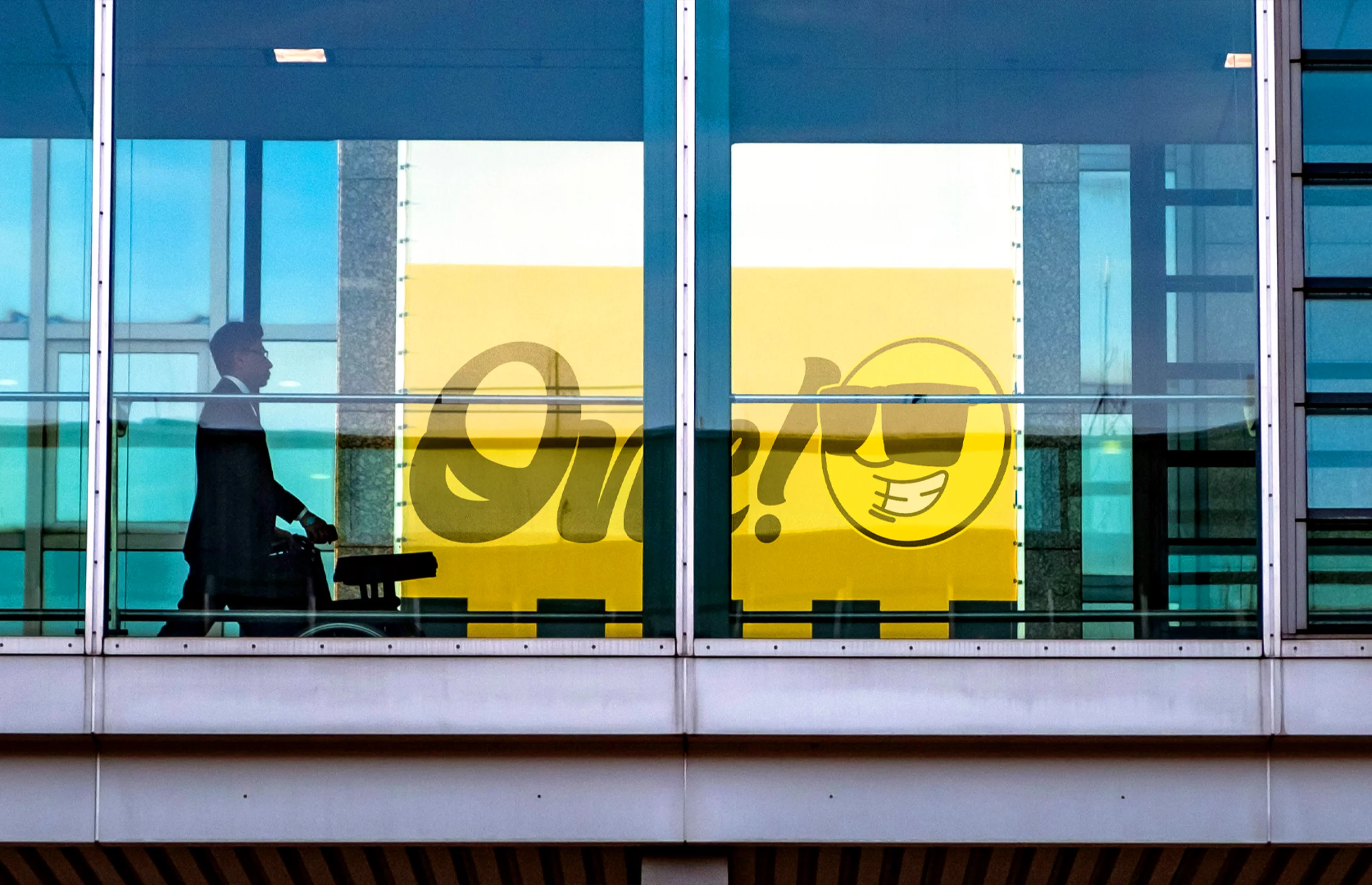 Publicidad de One Car Rental en un puente de aeropuerto, resaltando su branding vibrante y su presencia en el mercado de renta de autos turísticos.